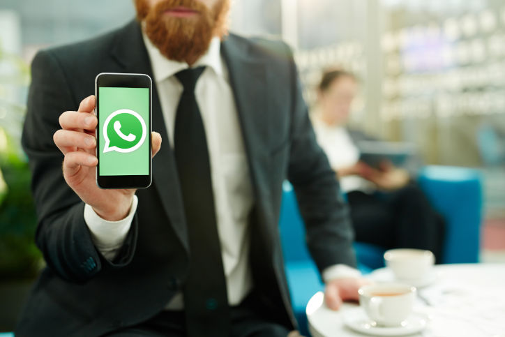 Um homem ruivo de terno segurando um smartphone com a logo do WhatsApp