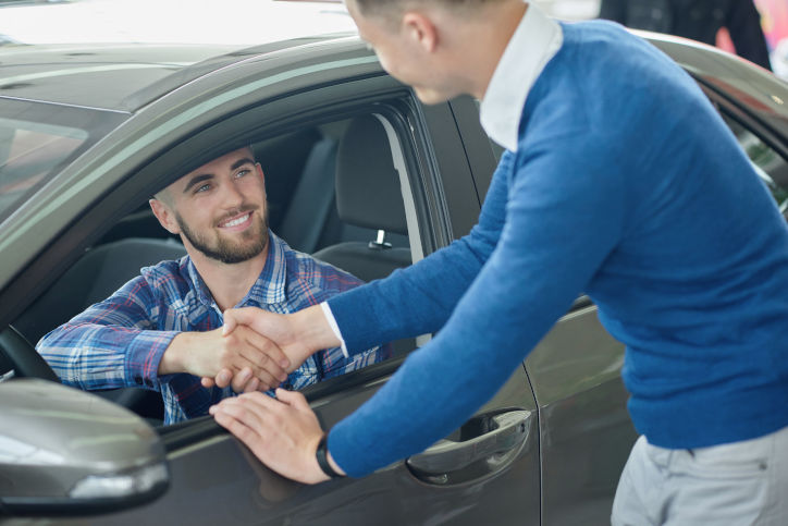 homem de sueter azul vendendo apertando a mão de um rapaz dentro de um carro após a venda