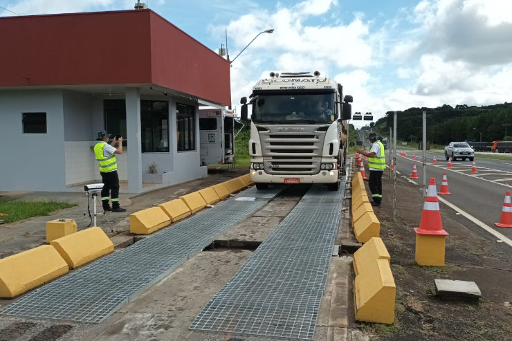 Caminhão branco sendo pesado em uma balança na rodovia