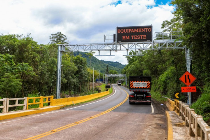 Estrada com um caminhão passando por um pórtico de pedágio free flow