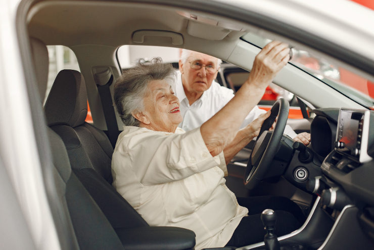 casal de idosos vendo um carro, a mulher está dentro do carro, enquanto o homem está do lado de fora olhando para dentro